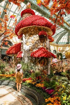 a woman in a pink hat is walking through a flower garden with a house shaped like a mushroom