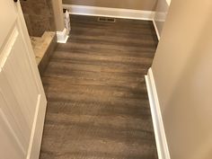 an empty hallway with wood flooring and white trim on the walls, next to a door