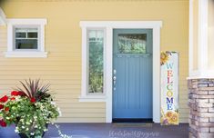 a blue front door on a yellow house with two potted plants in the foreground