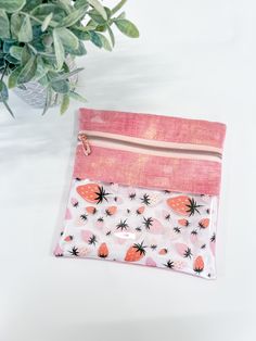 a pink and white pouch with strawberries on it next to a potted plant