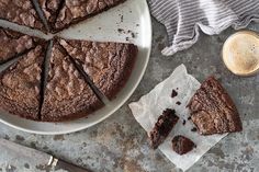 a chocolate cake on a plate with one slice cut out and two cups of coffee next to it