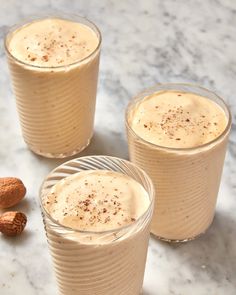 three glasses filled with pudding sitting on top of a marble table next to almonds