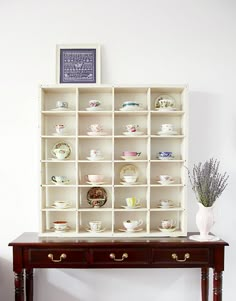 a shelf filled with cups and saucers on top of a wooden table next to a vase