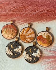 four embroidered pendants with designs on them sitting next to pink feathers and an orange feather