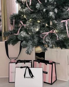 two shopping bags under a christmas tree with pink ribbons on them and one bag in front of it