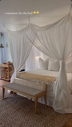 a bed with white drapes on top of it and a bench in front of it