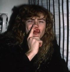 a woman with long curly hair is making a finger gesture to her lips while standing in front of a striped wall