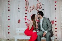 a man and woman sitting on a bench in front of a backdrop with love letters