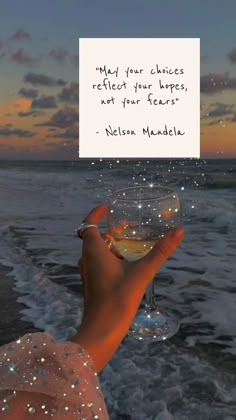 a person holding a wine glass in front of the ocean with a quote on it