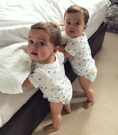 two toddlers standing on top of a bed next to each other and looking at the camera