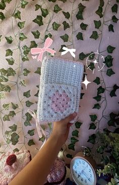 a person holding up a crocheted purse next to a clock and wallpaper