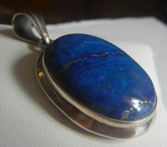 Sterling silver and lapis pendant.  Gorgeous, domed lapis cabochon with gold matrix set in a double bezeled setting.  A beautiful thick piece of lapis, well polished to show the rich royal blue color.  The tapered bail has a raised center line.  The back is open and framed, showing the same gold matrix as seen on the front of the stone.  An exceptional piece, solid weight over an ounce, and in excellent condition.  Please see detailed measurements below. >  Pendant weighs 17.6 grams. >  Sterling silver 925. >  Lapis lazuli. Measurements: >  Overall height including bail:  2". >  Pendant height not including bail:  1-1/2". >  Width:    just under 1-1/8". >  Depth/thickness:    3/8". >  Lapis measures  1-1/4" x 1". >  Back width of frame:  1/8". >  Bail:   1/2" x 5/16" tapering to 1/16". > Lapis Pendant, Lapis Lazuli Jewelry, Royal Blue Color, Cabochon Pendant, Matrix, Lapis Lazuli, Sterling Silver Pendants, Silver Jewelry, Jewelry Necklace Pendant