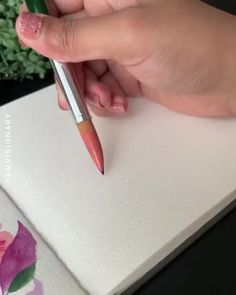 a person holding a pen and writing on a piece of paper with flowers in the background