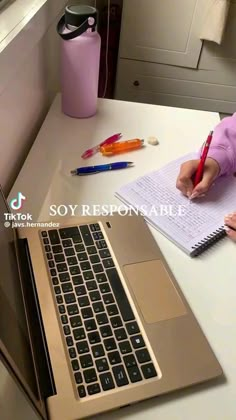 a person sitting at a desk with a laptop and notebook in front of them, writing on a piece of paper