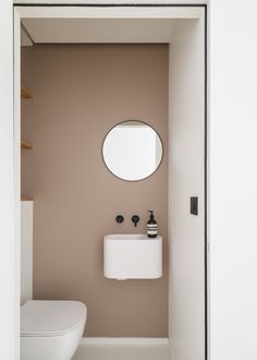 a white toilet sitting next to a bathroom sink under a round mirror on the wall