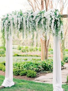 an outdoor wedding ceremony with white flowers and greenery on the top of the arch