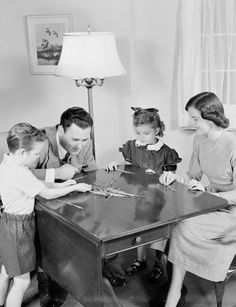 an old black and white photo of three people playing with scissors at a table in a living room