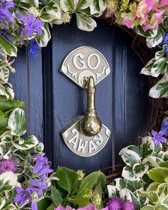 a blue door surrounded by flowers and greenery with a brass spoon in the center