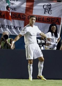 a man standing on top of a field holding a soccer ball in his hand and people behind him