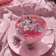 a pink drink being poured into a white cup with silver flowers on the rim and saucer