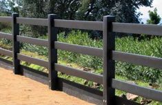 a wooden fence with black posts and grass in the background