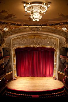 an empty theater stage with red curtains and chandelier hanging from the ceiling,