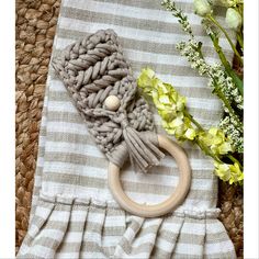 a gray and white blanket with a wooden ring on it next to some yellow flowers