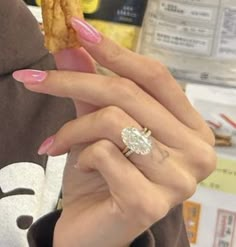 a woman with pink nails holds up a piece of food in her hand while wearing a ring