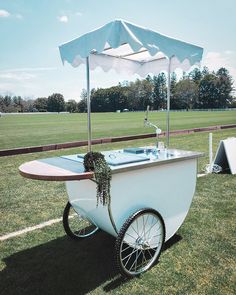 an old fashioned ice cream cart in the middle of a grassy field with umbrellas over it