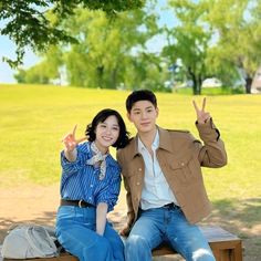 a man and woman sitting on a park bench giving the peace sign