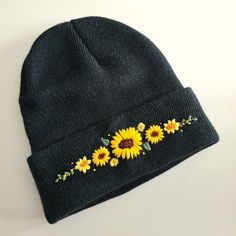 a black beanie with sunflowers embroidered on the front and side, sitting on a white surface