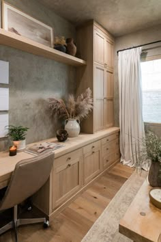 a room with a desk, shelves and plants on it in front of a window