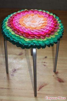 a multicolored crocheted stool sits on a wooden floor with metal legs