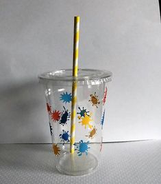 a plastic cup with a yellow straw sticking out of it's top and colorful splatters on the bottom