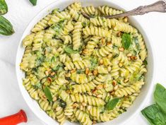 a white bowl filled with pasta and spinach on top of a table next to two spoons