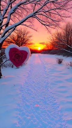 a heart - shaped object is in the middle of a snow covered path at sunset