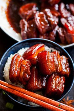 two bowls filled with meat and rice next to chopsticks on a table top