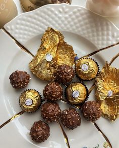 some chocolates are on a white plate with gold foiled leaves and candy sticks