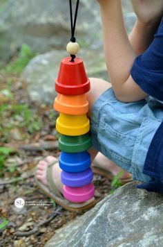 a child is playing with a stack of colorful wooden toys on a rock in the woods