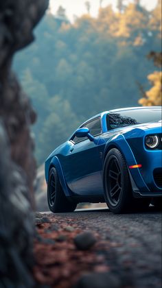 a blue sports car driving down a road next to some rocks and trees in the background