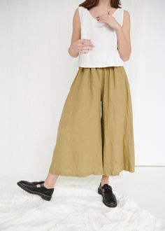 "The Clementine palazzo is the right choice for warmer days when you want to give a romantic touch to your look. The pants boast a cropped hem, in-seam pockets and a flattering gathered skirt-like high waist with an elastic band in the back. IMPORTANT: The Clementine pants have been altered to have a gathered waist instead of the pleated one. If you own a pair with pleated front, note that the pants you will receive will be different. This garment is true to size, and we recommend choosing the s Chic Olive Summer Pants, Olive Spring Trousers, Spring Olive Trousers, Chic Olive Bottoms For Summer, Chic Olive Pants For Spring, Olive Wide-leg Spring Pants, Olive Wide-leg Pants For Spring, Olive Linen Bottoms With Pockets, Olive Wide Leg Summer Bottoms