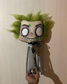 a hand holding a creepy doll with green hair on it's head and eyes