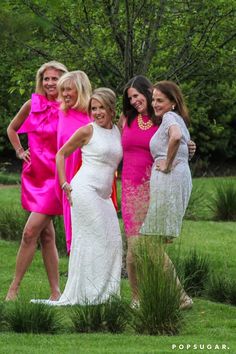 the women are posing for a photo together in front of some trees and bushes, all dressed in bright pink