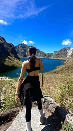 a woman sitting on top of a rock next to a body of water with mountains in the background