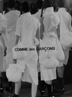 a woman walking down a runway with white dresses on her back and the words comme des garcos written in french