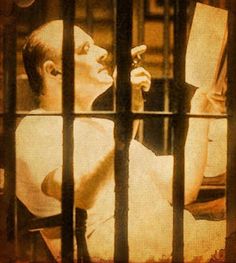 a man sitting in a jail cell holding a book and looking at something through the bars