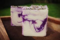 two purple and white soap bars sitting on top of a wooden tray