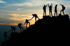 silhouettes of people holding hands on top of a mountain at sunset or dawn with the sun setting behind them