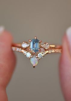 a woman's hand holding a ring with an aqua and white diamond in it