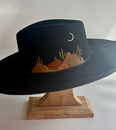 An ode to Saguaro National Park in Tucson AZ, this is one of my most liked designs revisited in new colors. They are already embroidered and ready to ship immediately! The hat is hand embroidered and there are two hat options: The first has a pencil-curled brim width of 4" and the second has a flat brim with width of 3.75". Both have an teardrop shaped crown with front pinches, a satin interior lining and an adjustable one-size-fits-most sweatband. This hat should fit anyone with a head circumference (where you wear a hat) of 23.25" and under. Embroidered Fedora Hat, Hand Painted Hats For Women, Wool Brimmed Hats, Hat Design Ideas, Hat Painting, Cowboy Hat Design, Hat Burning, Custom Cowboy Hats, Hat Bar